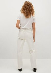 Bílé džínové kalhoty s vysokým pasem, rovný střih, pět kapsami a viditelnými švy. V kombinaci s bílou košilí s krátkým rukávem.