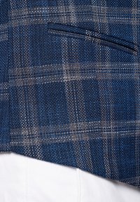 Niebieska tkanina w kratę z teksturowanym splotem i cienkimi białymi oraz brązowymi liniami, z małym detalem kieszeni. Biała tkanina widoczna poniżej.