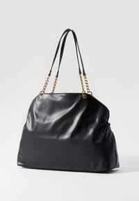 Large black leather handbag with a smooth texture, featuring two black straps and gold chain accents at attachment points.
