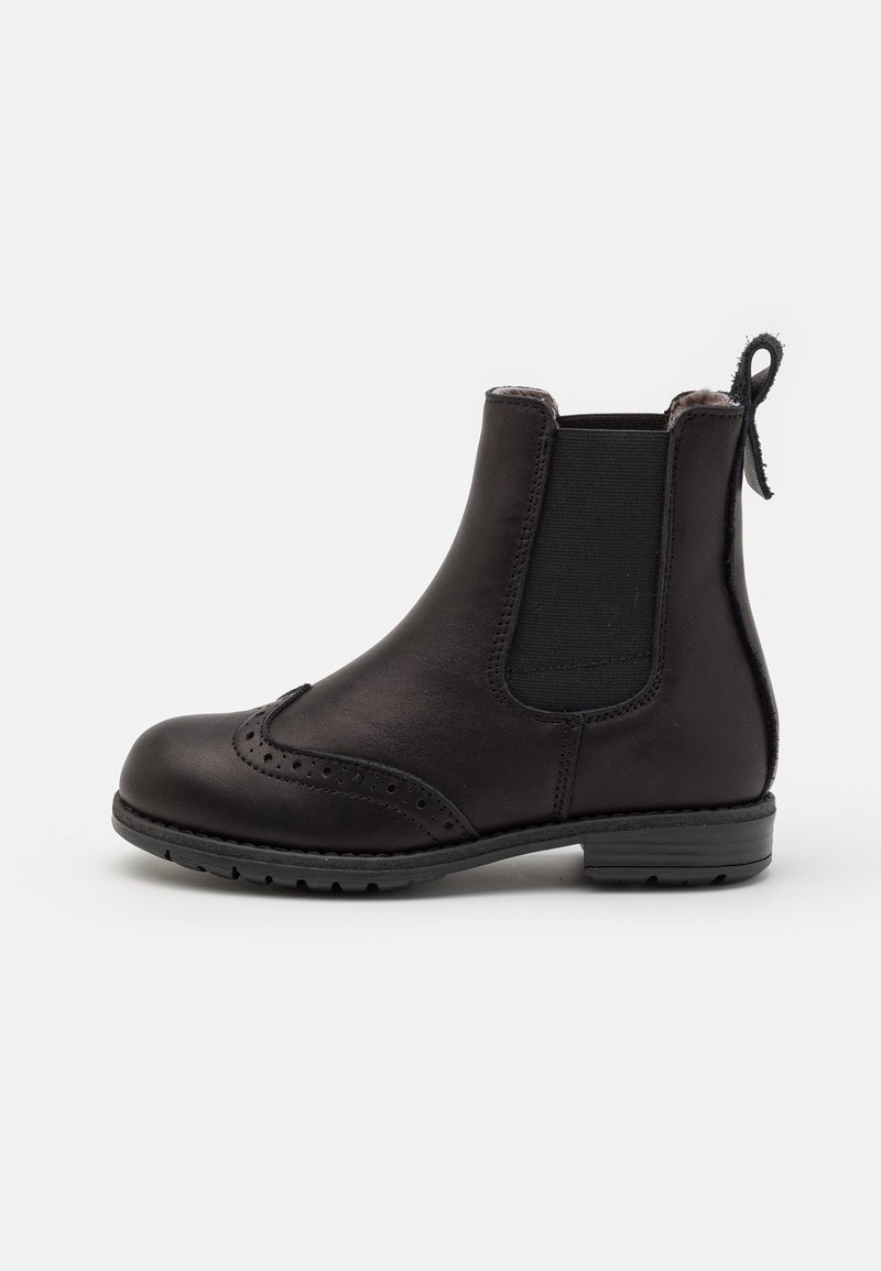 Botte Chelsea en cuir noir avec panneaux latéraux élastiques, détails brogue sur le bout, languette au talon et petit talon empilé, sur fond blanc.
