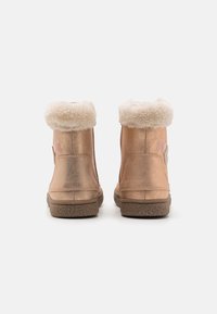 Botas de tobillo en oro rosa con forro de piel sintética y suela de goma texturizada, que cuentan con un cierre lateral y un detalle decorativo de logo.