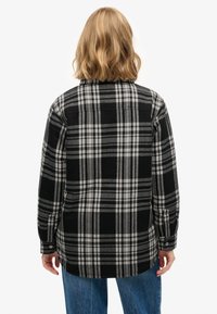 Black and white flannel shirt with a plaid pattern, long sleeves, buttoned cuffs, and a slightly curved hem, worn over blue jeans.