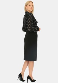 Czarna bluzka w kropki z falbaną, zestawiona z dopasowaną czarną spódnicą ołówkową i czarnymi szpilkami. Elegancka, profesjonalna sylwetka.