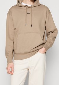 Sudadera beige con bolsillo canguro, capucha con cordón y logotipo negro "BOSS" en el pecho. Tejido suave con puños y dobladillo acanalados.