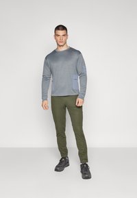 Gray long-sleeve shirt with blue accents and two front pockets, paired with olive green slim pants and black shoes. Smooth fabric texture.