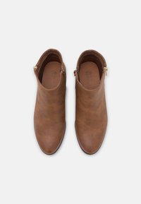 Ein Paar braune Leder-Ankle Boots mit seitlichen Reißverschlüssen, abgerundeten Spitzen und niedrigen Absätzen, von oben auf einem weißen Hintergrund gezeigt.