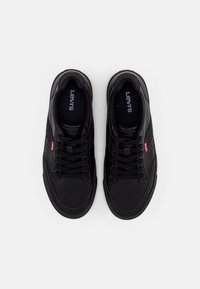 Baskets noires en matière synthétique avec embout rond, design à lacets, surface texturée, et un petit logo Levi's rouge sur le côté.