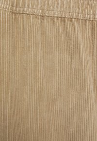 Béžová kordová tkanina s úzkymi vertikálnymi pruhmi, jemná textúra a elastický pás pre pohodlné nosenie.