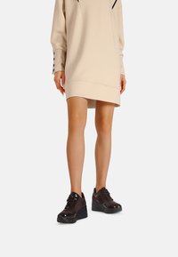 Calzature chunky in pelle marrone scuro con finitura lucida, dotate di lacci neri e suola texturizzata. Indossate con un vestito felpa beige.