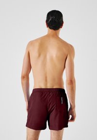 Bañador corto burdeos con cinturilla elástica y un bolsillo parche en el lado derecho. Material suave y ligero con un diseño sencillo.