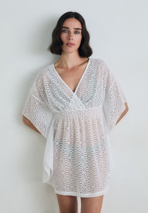 White lace dress with a V-neck, short sleeves, and an elastic waist. Features intricate oval patterns throughout. Lightweight and sheer fabric.