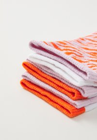 Pet pari čarapa složenih. Sadrže živopisne boje: narančasta, bijela i svijetlo ljubičasta. Neki su s teksturiranim uzorcima, dok su drugi glatki.