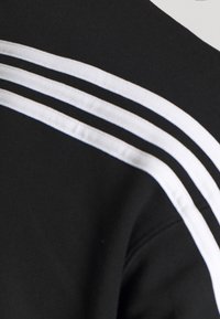 Czarna odzież z trzema białymi paskami wzdłuż szwu na ramieniu, wykonana z gładkiej tkaniny, z okrągłym dekoltem i dopasowanym krojem.