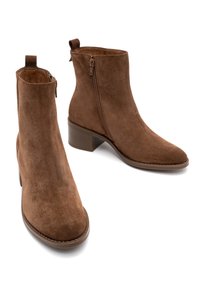 Brązowe zamszowe botki za kostkę na niskim słupku, z bocznym zamkiem błyskawicznym i pętelką do zakupu. Gładka faktura, zaokrąglony czubek i przeszycia na podeszwie.