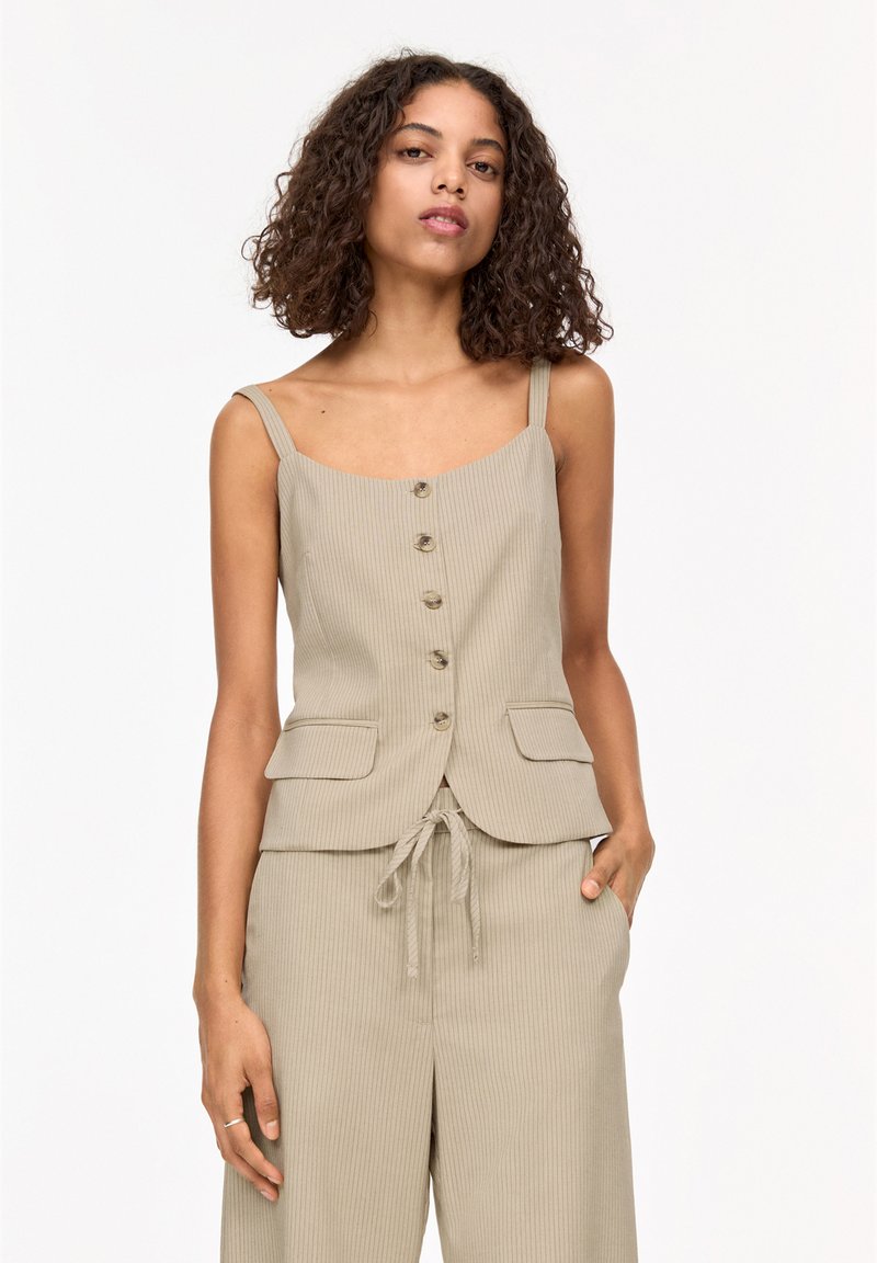 Débardeur beige côtelé avec des boutons sur le devant, des bretelles fines et deux poches avant, assorti à un pantalon large.