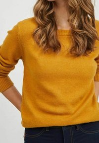 Pullover di maglia giallo senape con scollo rotondo, polsini a coste e vestibilità ampia; texture morbida, abbinato a jeans scuri.
