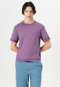 Purple short-sleeve t-shirt in soft cotton with contrasting stitching. Round neckline and a relaxed fit, paired with light blue denim pants.