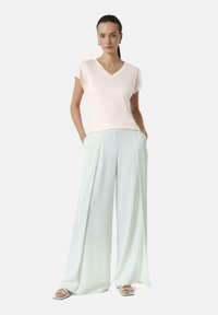 Lichtroze V-halstop met korte mouwen, gedragen bij mintgroene wijde broek met voorplooien. Model draagt witte bandjesandalen.