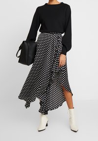 Top negro de manga larga combinado con una falda envolvente de lunares en blanco y negro con volantes, y botas blancas hasta el tobillo. Se incluye un bolso negro.