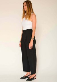 Pantalons noirs ajustés à taille haute avec des plis, associés à un débardeur blanc ajusté. Les chaussures ont un bout pointu avec des découpes.