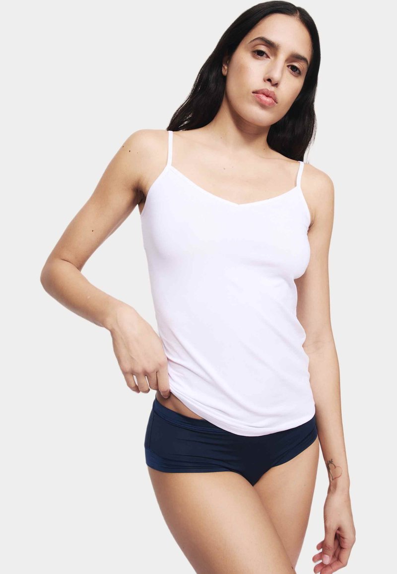 Camisola bianca con spalline sottili abbinata a pantaloni corti blu navy. Il tessuto appare liscio con un design aderente e uno stile minimalista.