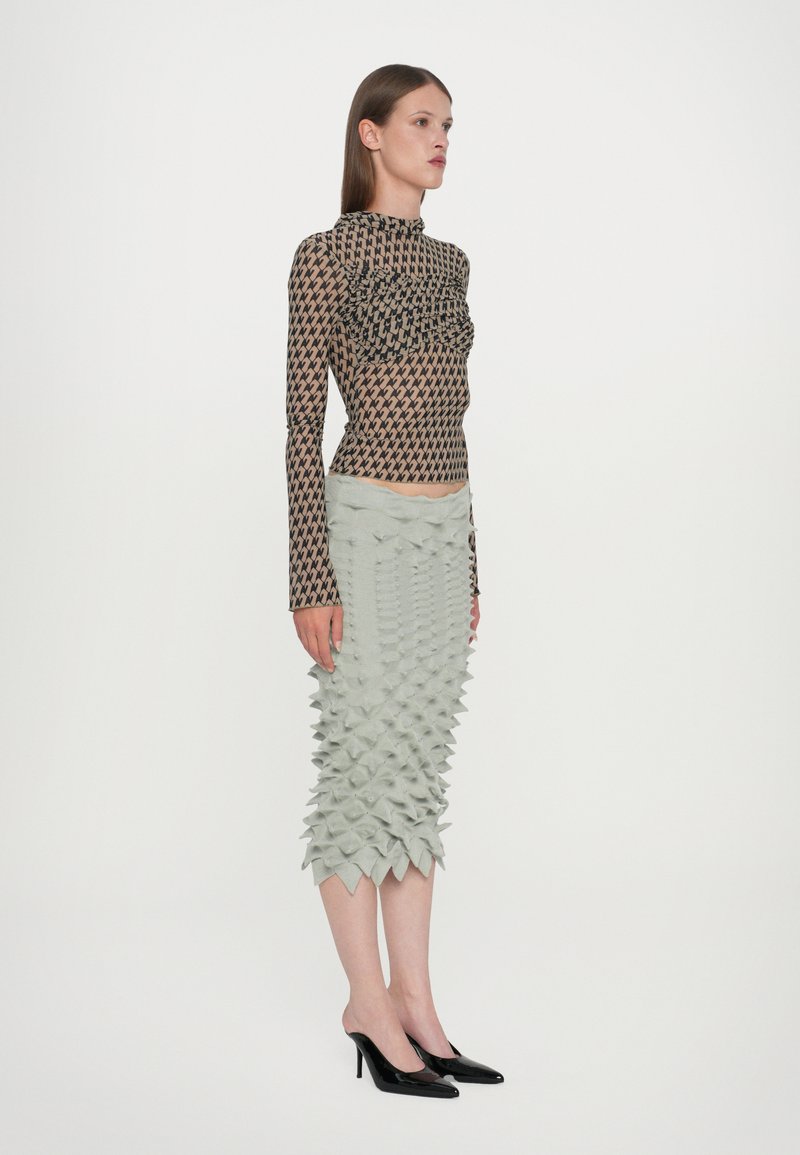 Langemouws T-shirt met een bruine geometrische print en ruches, gecombineerd met een lichtgrijze rok met driedimensionale spikes.