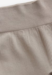 Beige geripptes Material mit einem breiten elastischen Bund. Die Textur ist weich und weist vertikale Linien sowie einen dezenten Glanz auf.