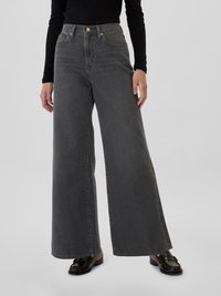 Jean en denim gris à jambes larges avec une taille haute, dotés de poches avant et de détails en laiton, associés à des mocassins noirs.
