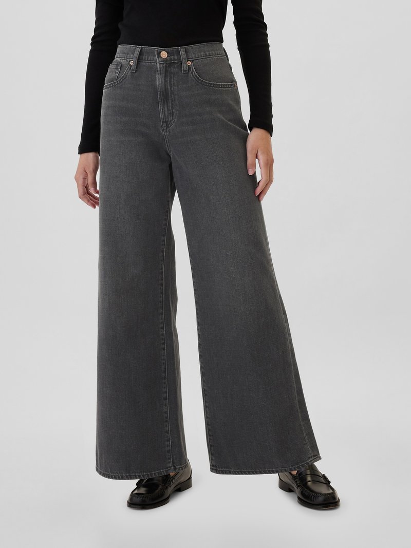 Jean en denim gris à jambes larges avec une taille haute, dotés de poches avant et de détails en laiton, associés à des mocassins noirs.