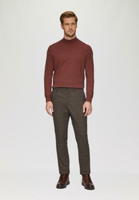 Bordeauxrode trui met hoge kraag, gecombineerd met bruine broek met ruitpatroon en bruine leren laarzen. Glad textuur, moderne snit.