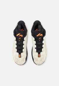 Et par beige og sorte sneakers med orange accenter, sorte snørebånd og trækflapper, vist fra ovenstående udsigt på en hvid baggrund.