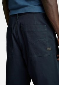 Navyblauwe cargobroek met twee grote zijzakken, contrasterende stiksels en een G-Star Originals-label nabij de tailleband.