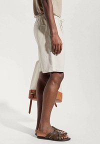 Shorts en lin beige avec une taille élastique, poches latérales et une coupe décontractée, associés à des sandales marron à brides.