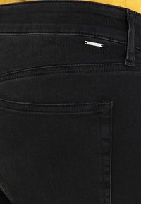 Jeans de mezclilla negros con un bolsillo trasero con detalle de costura y un pequeño acento en plata con el logo "DIESEL". Textura suave y diseño ajustado.