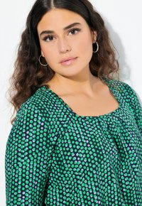 Top verde e blu a pois, realizzato in tessuto leggero, con scollatura rotonda e leggeri arricciature sul seno per una vestibilità rilassata.