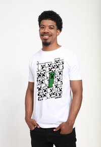 Bílý bavlněný tričko s grafickým designem z několika Minecraft hlav s výrazným zeleným Creeperem ve středu. Krátké rukávy.