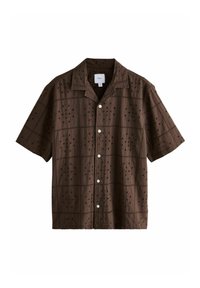 Chemise marron à manches courtes en tissu texturé, ornée de motifs brodés et de découpes décoratives, avec des boutons blancs et un col.