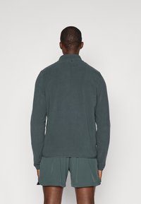 Ciemnozielona koszula z długim rękawem, wykonana z miękkiego materiału, z kołnierzykiem i detalami z guzikami, zestawiona z pasującymi szortami.