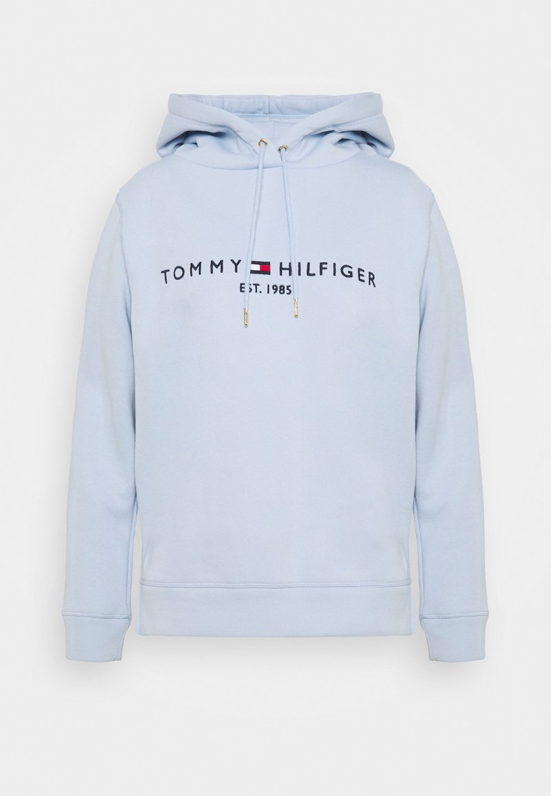 Hoodie bleu clair en tissu doux, avec un logo sur le devant indiquant "TOMMY HILFIGER" et "EST. 1985", des cordons de serrage ajustables et des poignets côtelés.