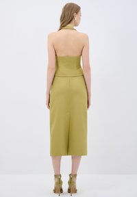 Olivgrünes Kleid mit passendem Neckholder, rückenfreiem Design und knielangem Rock. Das Model trägt beigefarbene Riemchen-Stilettos.