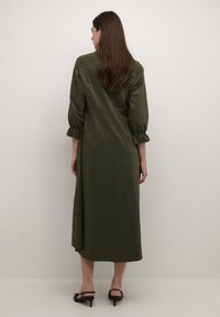 Olive green, mid-length dress with puffed sleeves, gathered cuffs, and a relaxed silhouette. Smooth texture and minimal design details.