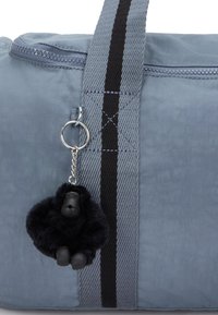 Harmaa kangaskassi mustilla raidoilla, vetoketjukiinnitys ja huomattava lisävarusteena karvainen musta gorillan avaimenperä.