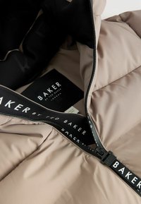 Puffjacke in hellbeige mit schwarzem Innenfutter und Markenlabel. Verfügt über einen schwarzen Reißverschluss mit einem Marken-Zipper und gestepptem Textil.