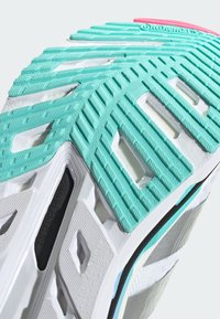 Sole della scarpa con un motivo testurizzato turchese e bianco, caratterizzata da scanalature e ritagli, e contrassegnata con "DISTANCE DRIVE" in nero.