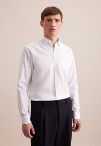 Witte blouse met lichtblauwe verticale strepen, lange mouwen en een linkerschouderzak, gecombineerd met donkere broeken. Vlotte textuur.