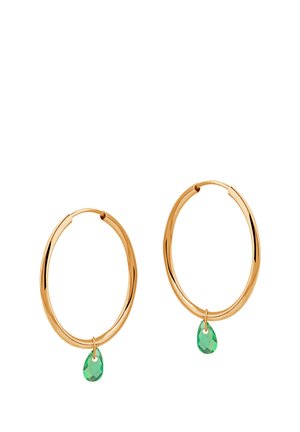 Złote kolczyki w kształcie kół z gładkim, okrągłym wzorem, z małym, zielonym kamieniem w kształcie łzy wiszącym z każdego kolczyka.