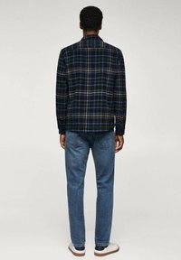 Navy, groene en gele geruite flanellen shirt met een ontspannen pasvorm en lange mouwen, gecombineerd met lichtblauwe denim jeans.