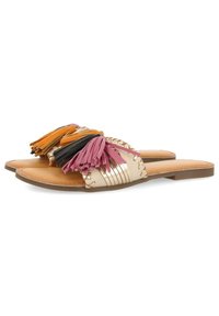 Platta sandaler med en beige läderbas, prydda med färgglada fransar i rosa, orange, svart och gult, tillsammans med randiga metallaccenter.