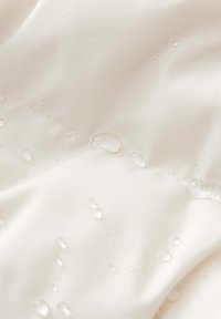 Tissu résistant à l'eau de couleur crème, présentant une texture lisse et des gouttes d'eau visibles sur la surface, mettant en avant sa qualité déperlant.