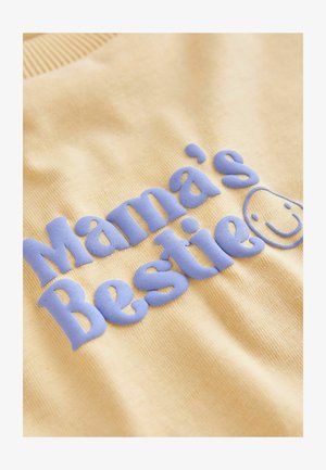 Keltainen pusero, jossa koholla sinisellä tekstillä "Mama's Bestie" ja hymyilevä kasvot, valmistettu pehmeästä kankaasta, jossa on resorinen pääntie.